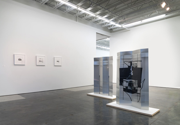 A contemporary gallery interior with polished concrete floors and white walls displaying three small framed stipple drawings on the left wall, and two large translucent blue-tinted sculptural panels on white pedestals in the center space, each containing gestural black marks and forms within their transparent surfaces.
